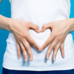 Woman holding a heart sign with hands at her stomach
